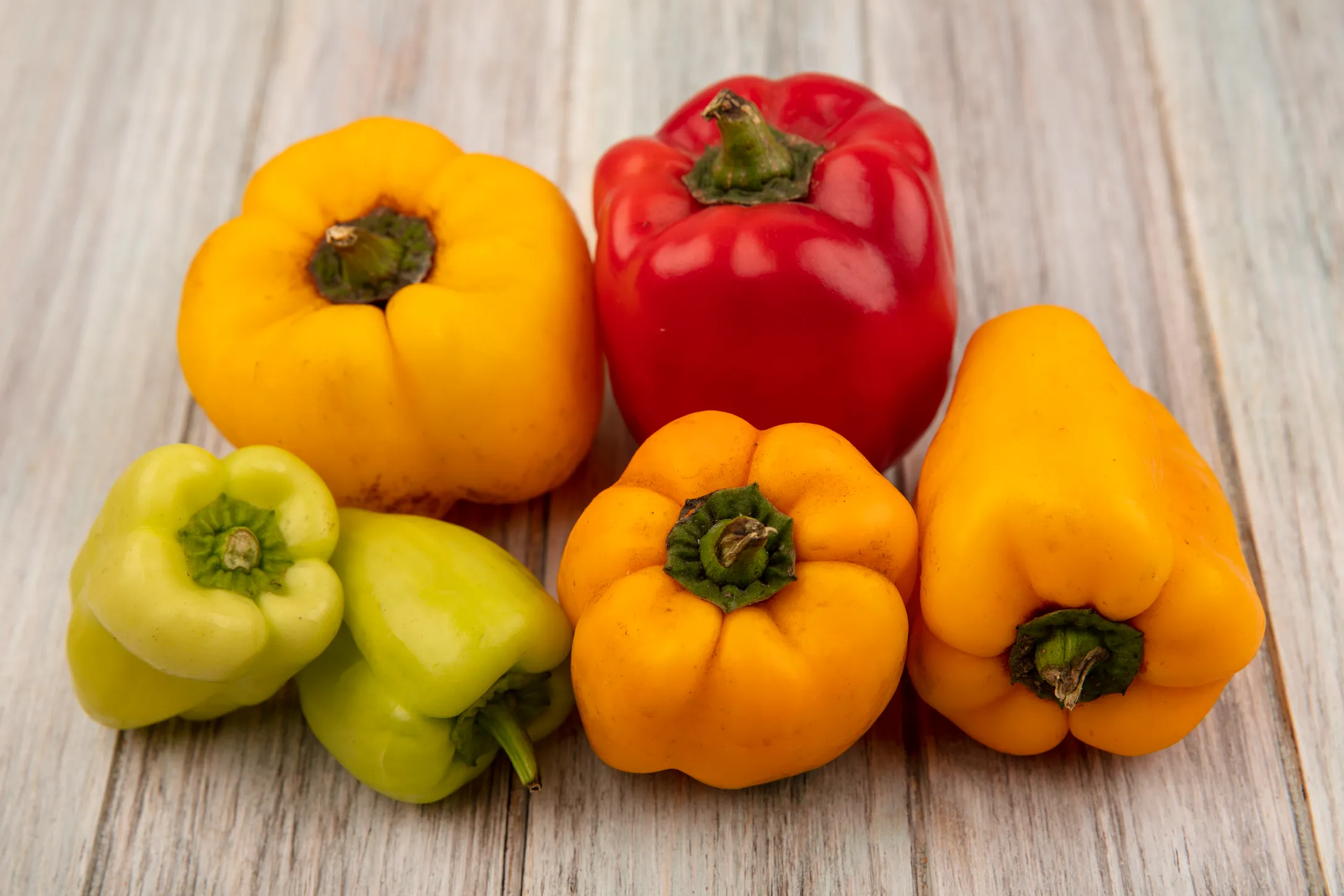 Yellow, red, and green peppers are grouped on a light surface, highlighting the diversity and vibrancy of their colors.
